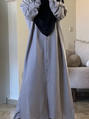 alt="طقم نسائي محتشم باللون الرمادي، قميص بأزرار خشبية وبنطال طويل وواسع مناسب للأجواء الحارة والمعتدلة"