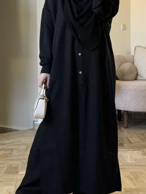 alt="طقم نسائي محتشم باللون الأسود، قميص بأزرار خشبية وبنطال طويل وواسع من قماش تايور خفيف"